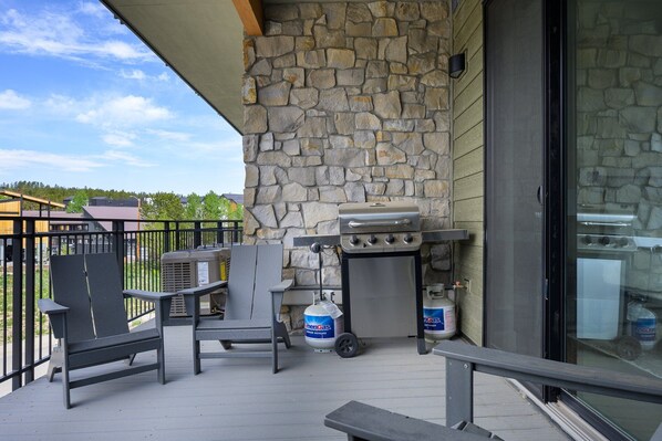 Un balcon avec un mur en pierre, un barbecue, une chaise et une table.