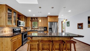 Una cocina moderna con armarios de madera, encimeras de granito, electrodomésticos de acero inoxidable y una zona de bar con taburetes.