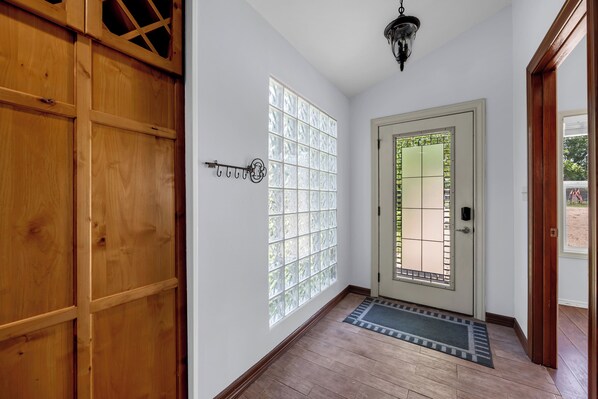 Un couloir doté d’un plancher en bois, une porte avec un panneau de verre et un luminaire suspendu.
