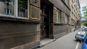 A building with a dark facade, a visible entrance, and a parked car on the adjacent street. - Komorowskiego Riverside Apartment (Kraków)