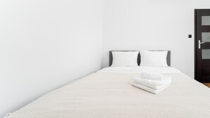 A minimalist hotel room with a single bed, white linens, and a neatly folded towel on the bed. - Komorowskiego Riverside Apartment (Kraków)