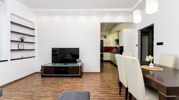 A modern living room with a flat-screen TV, wooden flooring, a dining table with chairs, and a kitchen visible in the background. - Komorowskiego Riverside Apartment (Kraków)