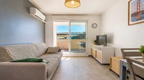 Un salon moderne comprenant un canapé, un téléviseur et un coin repas, avec une grande porte-fenêtre coulissante donnant sur un espace extérieur.