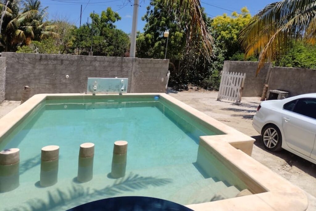 Uma piscina retangular com água azul cristalina, rodeada por um muro de pedra baixo.