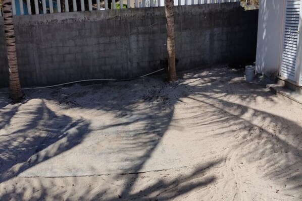 A concrete area with shadows cast by trees, a concrete wall, and a metal fence.