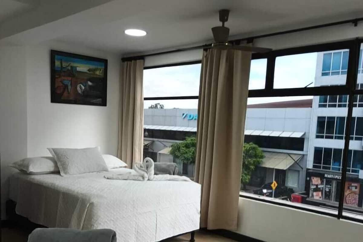 Ein Hotelzimmer mit zwei Betten, einem Bild an der Wand und Blick auf Gebäude.