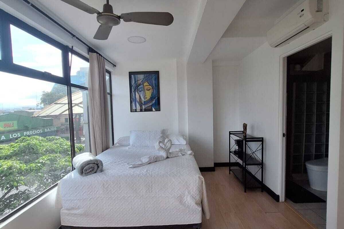 Ein geräumiges Schlafzimmer mit einem großen Bett, einem Deckenventilator, einem Fenster mit Ausblick und einem Bild an der Wand.