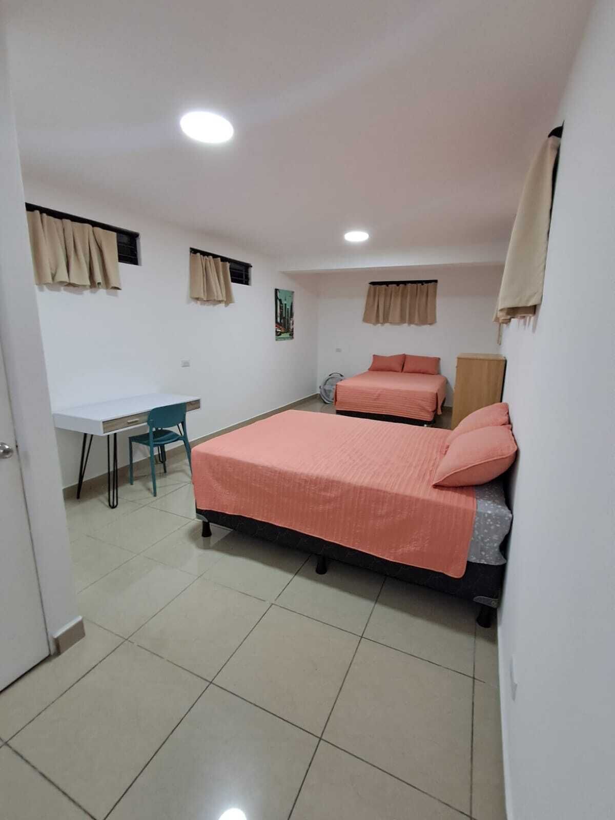 A bedroom with two beds, a desk, and a chair.