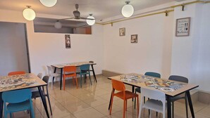 Un comedor con mesas y sillas, ventiladores de techo e iluminación en la pared.