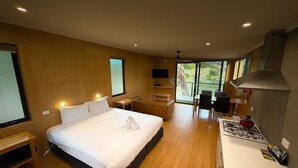 A modern hotel room with a large bed, a small desk, a seating area, and a kitchenette.