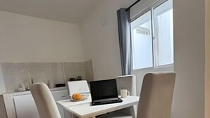 A small, modern room with a white desk, two chairs, a laptop, and a window with curtains.