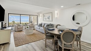 Een moderne woonkamer met een groot raam, een ronde spiegel en een eethoek met een tafel en stoelen.