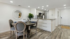 Een moderne keuken met witte kasten, een centraal eiland en een eetgedeelte met een ronde tafel en stoelen.