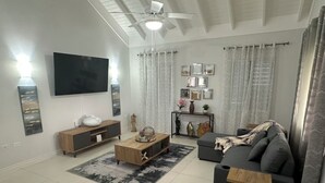 Ett modernt vardagsrum med en platt-TV, trämöbler, en grå soffa och en takfläkt.