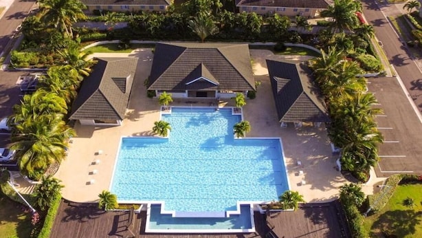 Ett flygbildsfoto av ett semesterområde med en central pool, flera byggnader i bungalowstil och omgivande palmer.