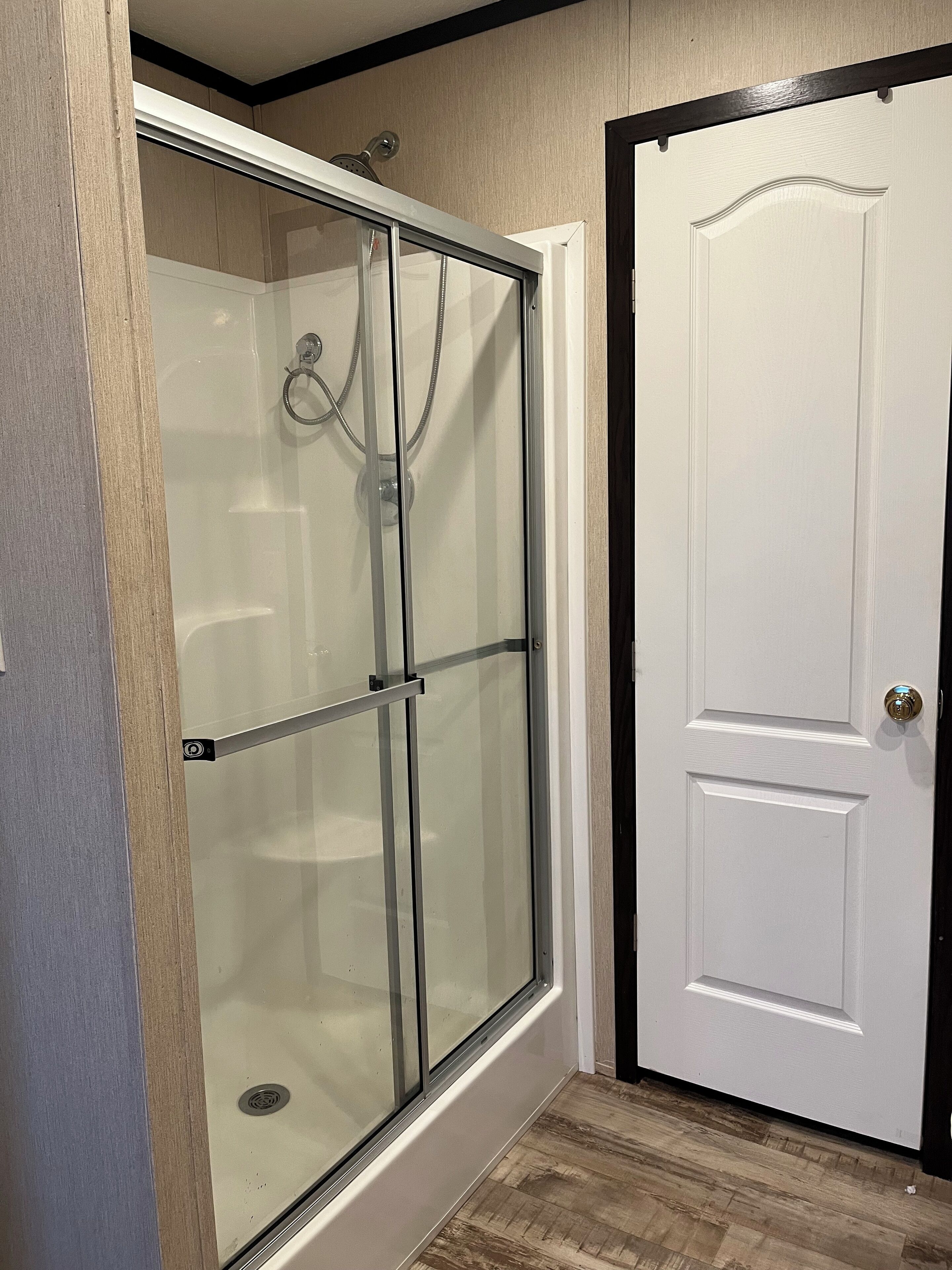 Un baño con ducha de vidrio, puerta blanca y suelo de madera.
