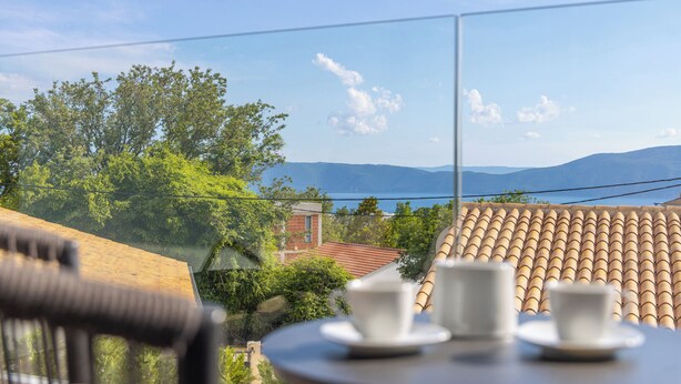 Ein Balkon mit Tisch und Stühlen, mit Blick auf eine malerische Seen- und Berglandschaft.