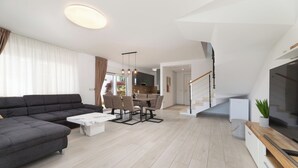 Ein modernes Wohnzimmer mit einem Ecksofa, einem Esstisch mit Stühlen und einer Küche im Hintergrund.