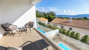 Ein Balkon mit Pool, Gartenmöbeln und Blick auf das Meer und Gebäude.