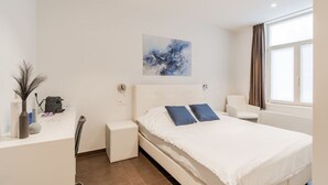 A modern hotel room with a large bed, a desk with a chair, a small table, and a window with curtains. - Elegant room with private bathroom near city center (Brugge)