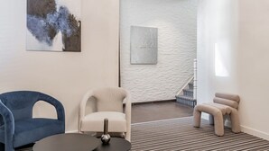 A modern room with a blue chair, a beige armchair, and a small stool. There is a painting on the wall and a staircase in the background. - Elegant room with private bathroom near city center (Brugge)