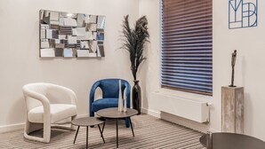 A modern room with a white armchair, a blue armchair, a small table, a decorative mirror, and a window with blinds. - Elegant room with private bathroom near city center (Brugge)