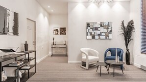 A modern living room with a black and white striped carpet, a white armchair, a blue armchair, a small round table, and a black console table with shelves. - Luxury two-room suite with balcony near city center (Brugge)