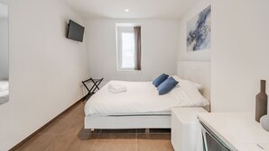 Una habitación de hotel moderna con una cama, un televisor de pantalla plana, un ventanal con cortinas, un cuadro en la pared y un escritorio pequeño con un jarrón.