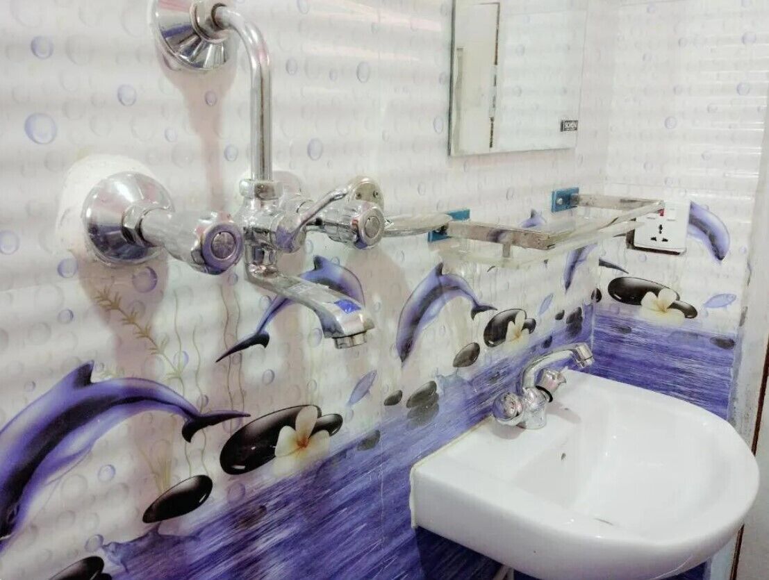 Een badkamer met een witte wastafel, een spiegel en een douche met glazen deur. Op de muur zijn decoratieve elementen te zien, waaronder een muurschildering van een dolfijn.