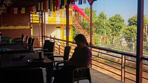 Um restaurante com mesas ao ar livre, parede de tijolos e bandeiras coloridas.