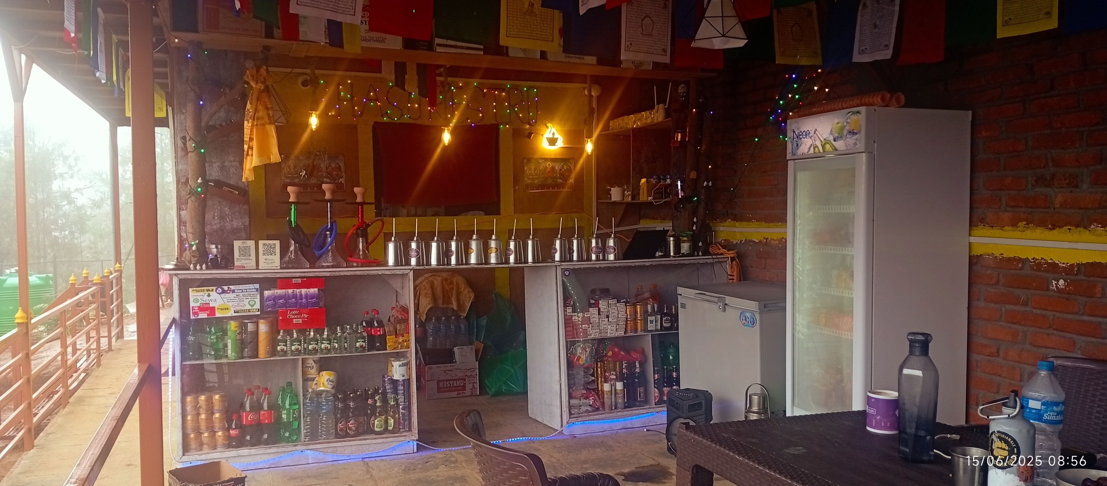 Un espace bar équipé d’un réfrigérateur, d’étagères remplies de boissons et d’un coin salon avec une table et des chaises.