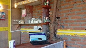 Um quarto rústico com parede de tijolos, uma prateleira de madeira com utensílios de cozinha, um laptop sobre uma mesa e um quadro pendurado na parede.