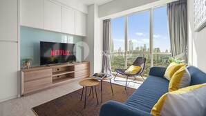 A modern living room with a large TV, a sofa, a chair, and a view of the city. - Dovra by Kozystay - Kuningan (Jakarta)