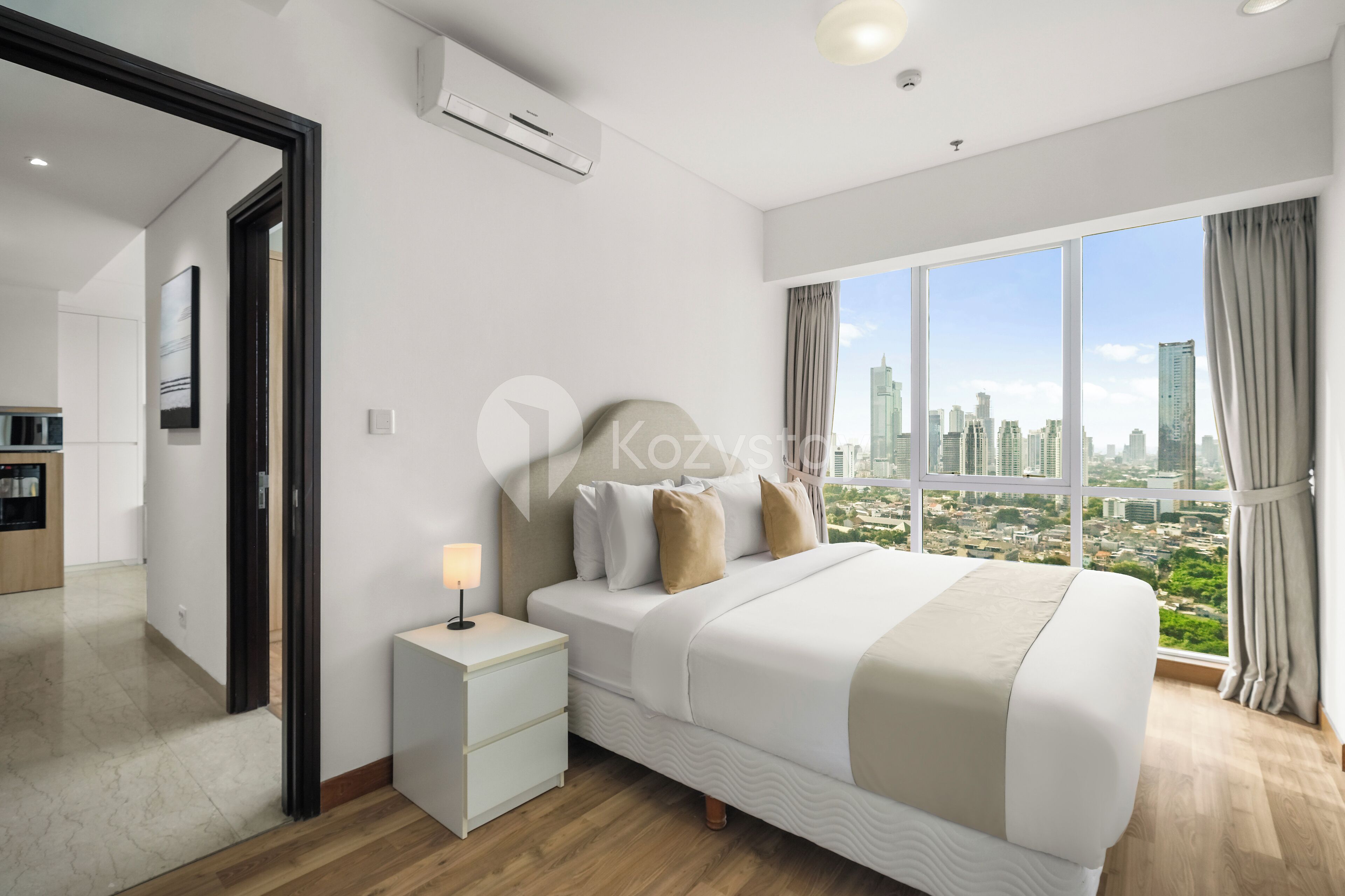 Une chambre d’hôtel moderne avec un grand lit, une table de chevet et une vue sur le paysage urbain grâce à de grandes fenêtres.