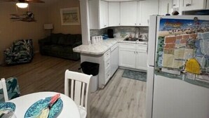Une cuisine compacte avec des meubles blancs, un réfrigérateur décoré d’une carte, une table à manger avec des chaises et un ventilateur de plafond.