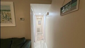 Un couloir étroit, avec un canapé vert sur la gauche, un thermostat au mur et un panneau indiquant « Plage » sur la droite.