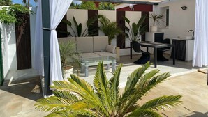 A covered outdoor seating area with a sofa and dining table, surrounded by potted plants and a pergola. - Rincón Vacacional Les Rotes 53 · Near de sea (Unknown)