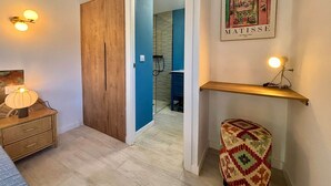 A room with a wooden wardrobe, a small stool, a wall-mounted shelf with a lamp, and a framed artwork. - Rincón Vacacional Les Rotes 53 · Near de sea (Unknown)