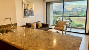 Una cocina moderna con encimera de granito, un sofá con cojines, una silla y un ventanal con vistas a un paisaje verde.