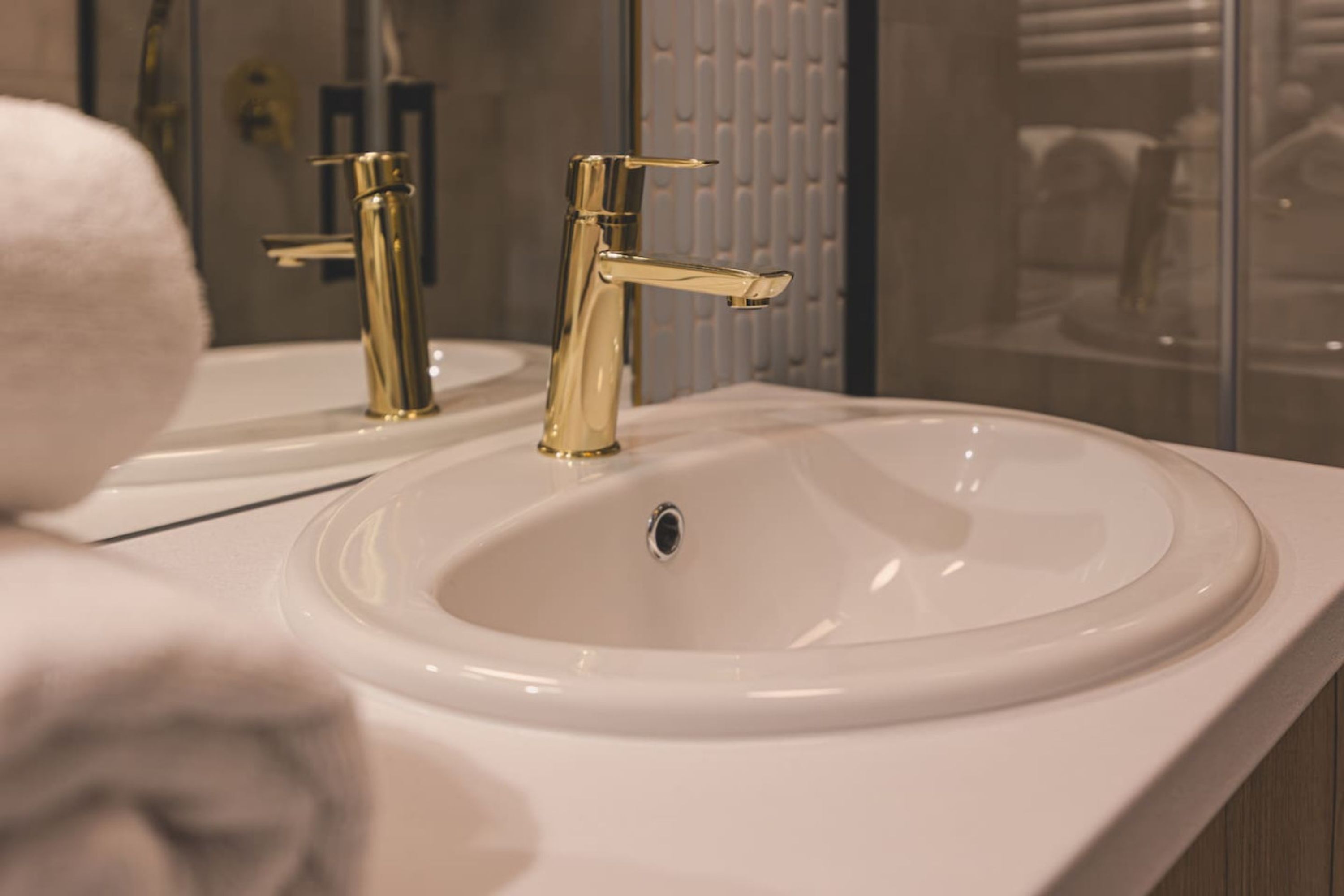 A bathroom with a white sink, gold faucets, and a mirror.
