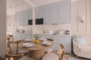A modern kitchen with light blue cabinets, a round dining table set for four, and a beige sofa in the background. - Aura Nowy Port Przytulne Studio Przy Operze (Bydgoszcz)