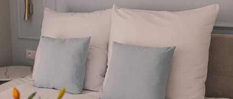 A bed with white bedding and two light blue pillows.