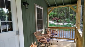 A wooden porch with two wicker chairs and a metal bucket filled with wooden planks.