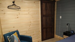 A room with a wooden slat wall, a blue chair, a bed with a blue bedspread, and a wooden door.