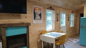 A cozy cabin interior with a wooden interior, a fireplace, a dining table with chairs, and a vintage refrigerator.