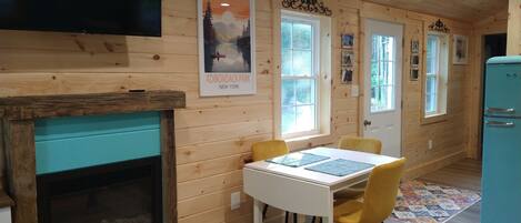 A cozy cabin interior with a wooden interior, a fireplace, a dining table with chairs, and a vintage refrigerator.