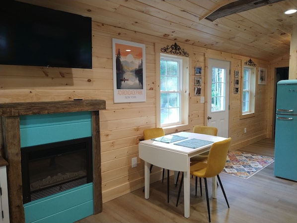 A cozy cabin interior with a wooden interior, a fireplace, a dining table with chairs, and a vintage refrigerator.