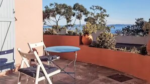 Eine Terrasse mit Tisch und Stühlen, mit Blick auf eine malerische Landschaft aus Bäumen und dem Meer.