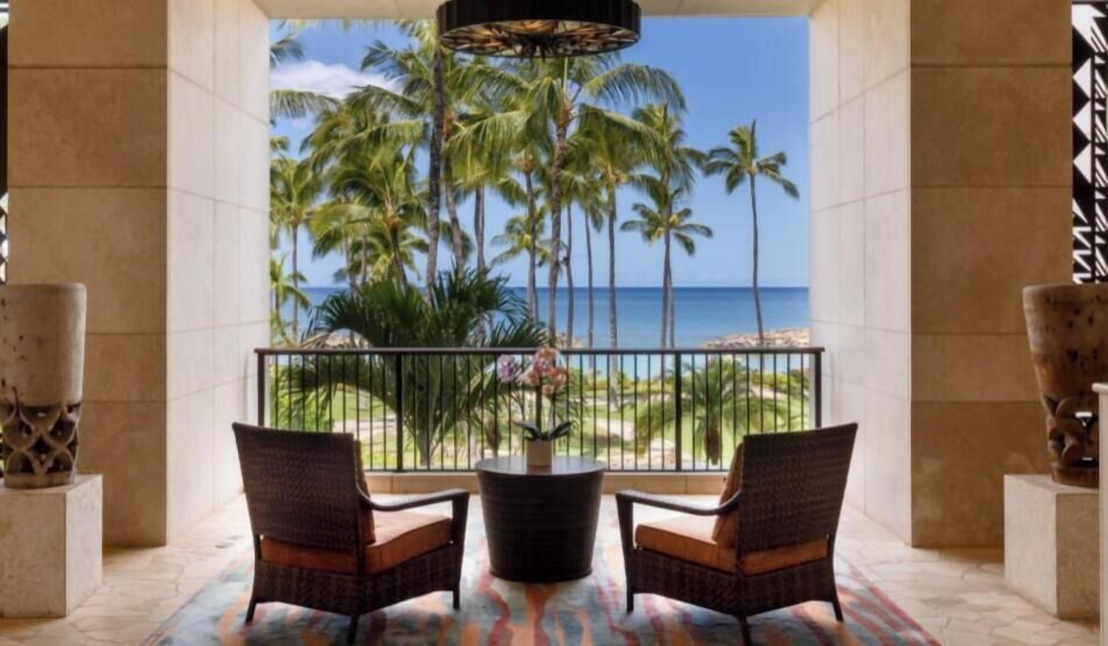 A balcony with wicker chairs, a central table, and a view of the ocean and palm trees.