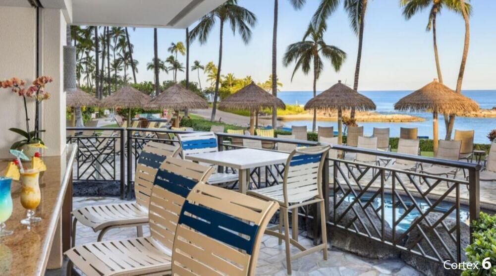 En resort-terrasse med udendørs møbler, en pool og udsigt til stranden og havet.